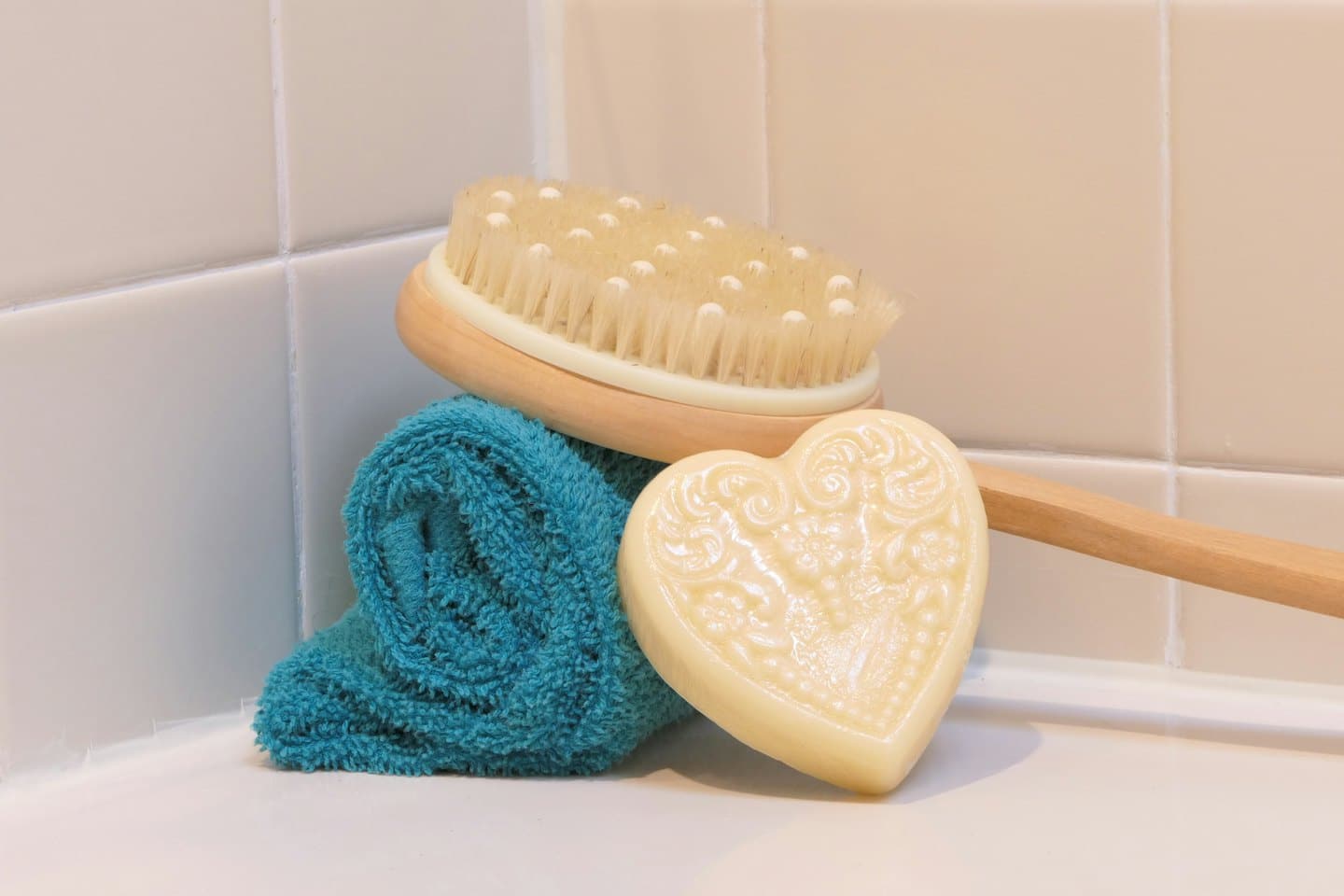 Wooden body brush, teal towel, and soap on white surface.