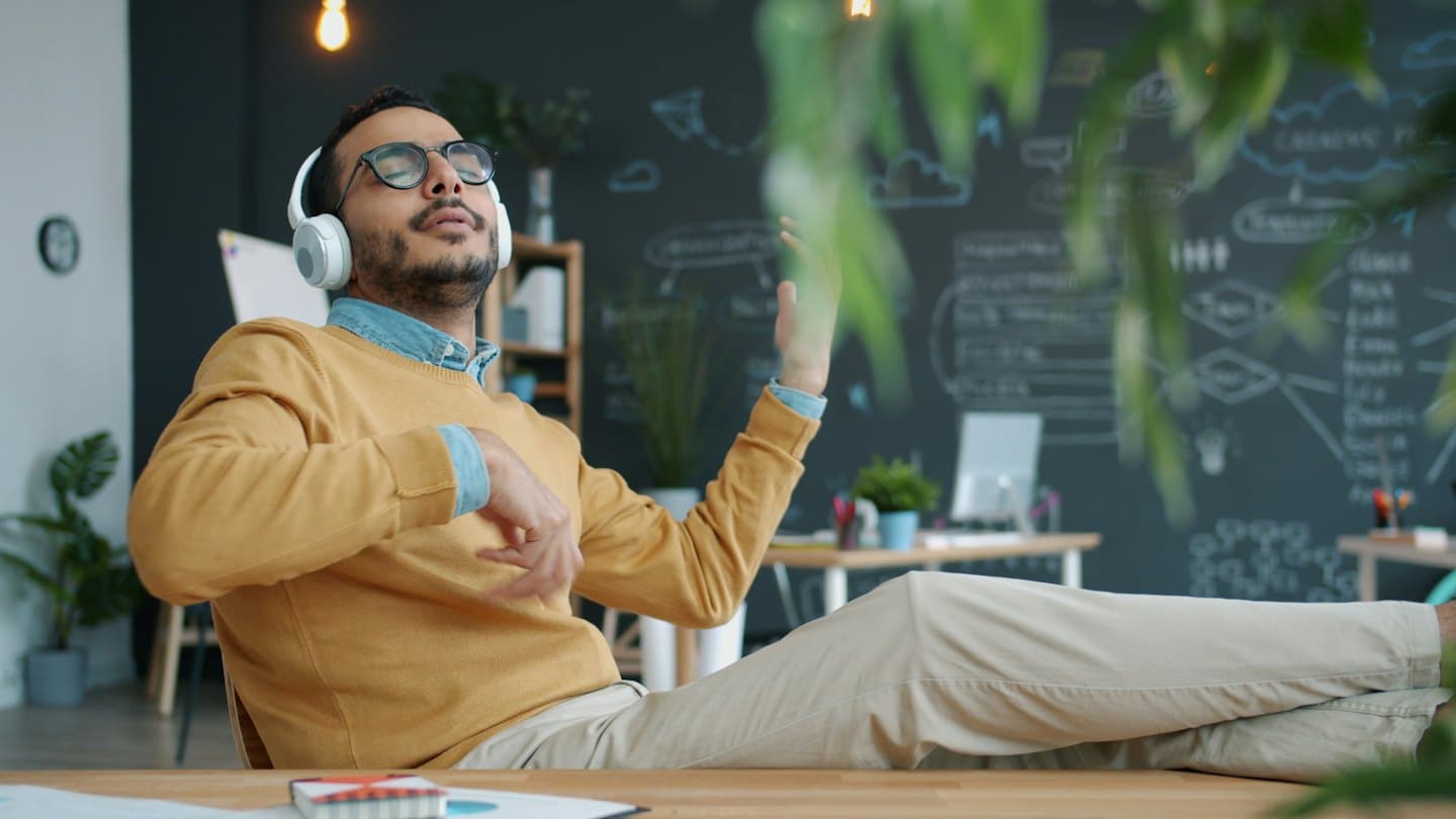 Man in a yellow sweater listens to music while sitting in an office.