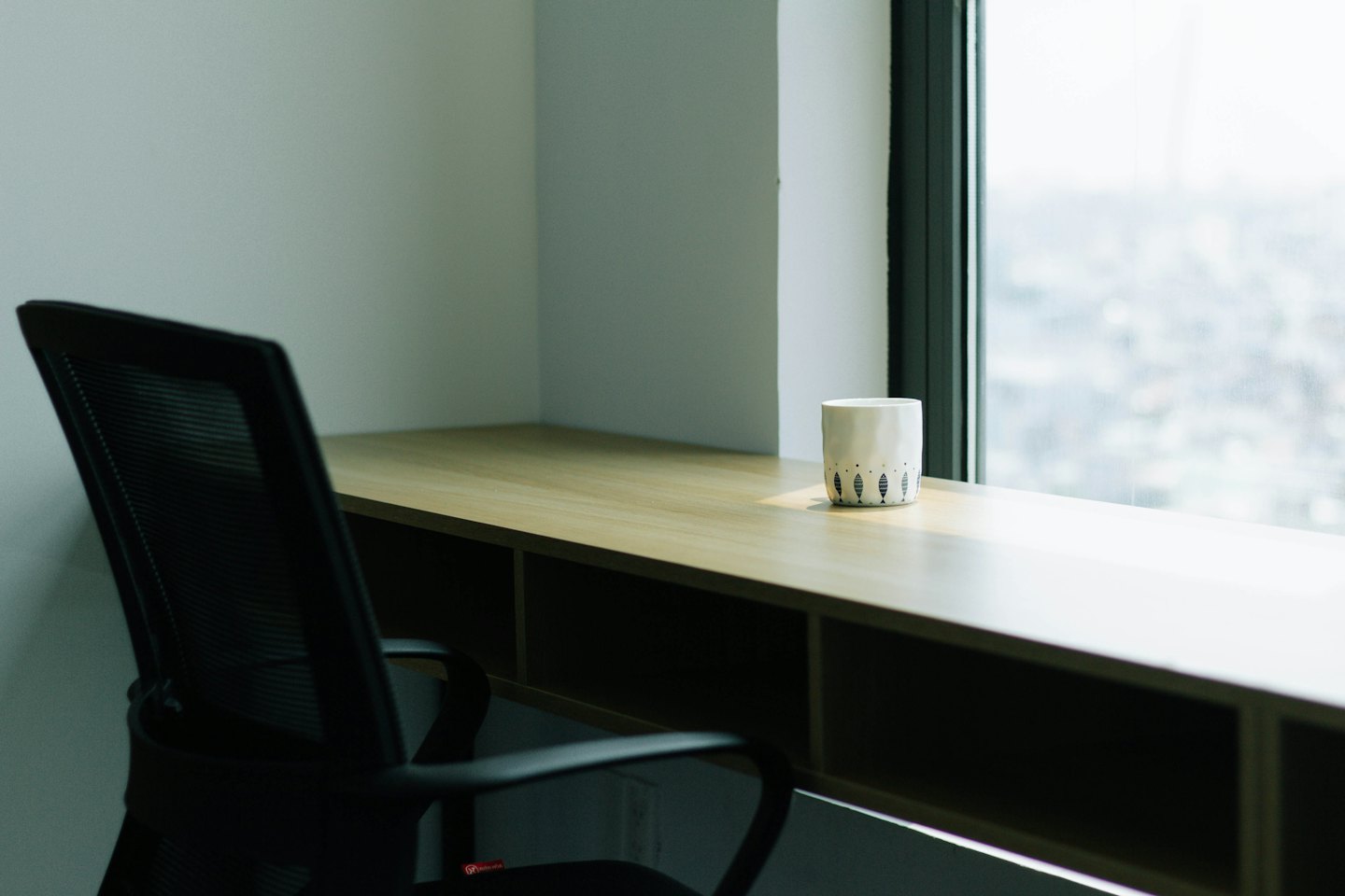 Black office chair sits beside a wooden desk with a mug.